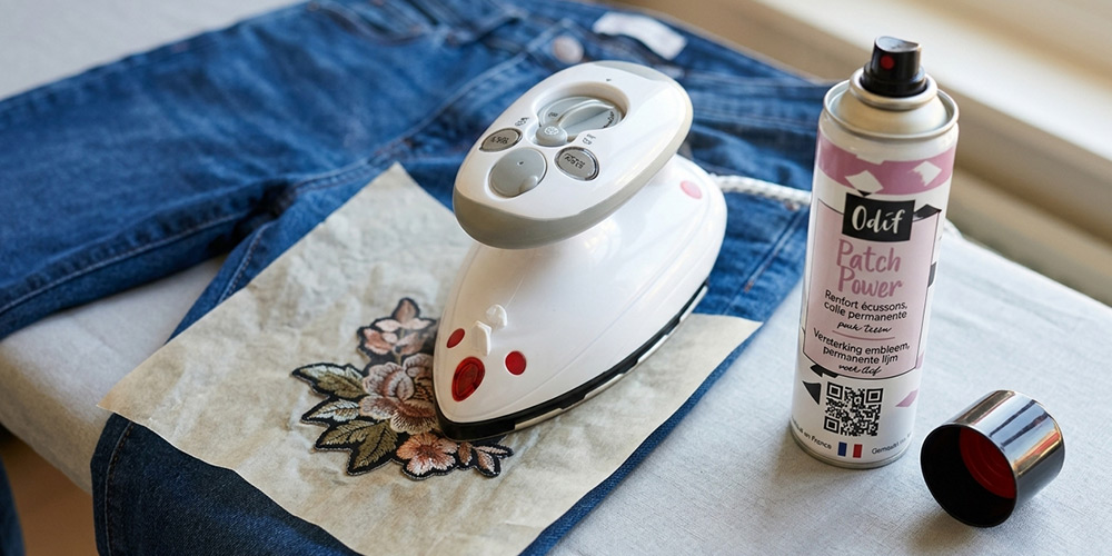 Écusson brodé posé sur un jean, fer à repasser et papier sulfurisé : fixation d'un patch à la colle thermocollante