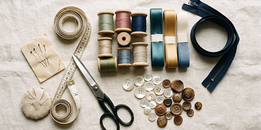 Fournitures de mercerie disposées sur une table : bobines de fil, boutons, fermetures à glissière, rubans, ciseaux, aiguilles et mètre ruban